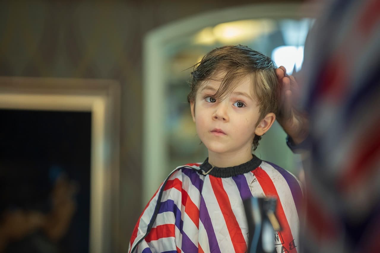 A young boy in a striped cape waiting for his haircut